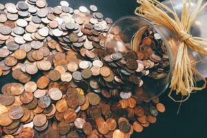 Glass jar spilling hundreds of copper coins onto a table, symbolising the high financial cost of workplace stress, employee burnout, and poor mental health on UK businesses and HR budgets
