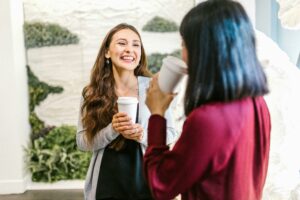Two female colleagues enjoying a coffee break at work, illustrating the importance of taking regular work breaks for employee wellbeing, reducing workplace stress, and boosting productivity in office environments.